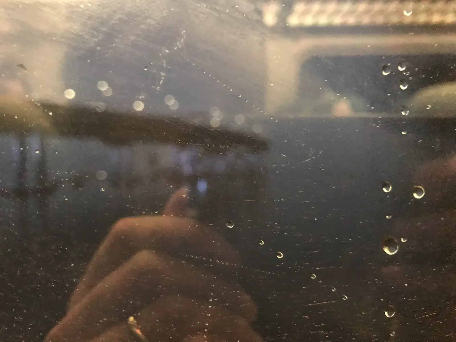 A rainy, slightly blurry view of the Mario Cuomo Bridge seen through a train window covered in water droplets and reflections.