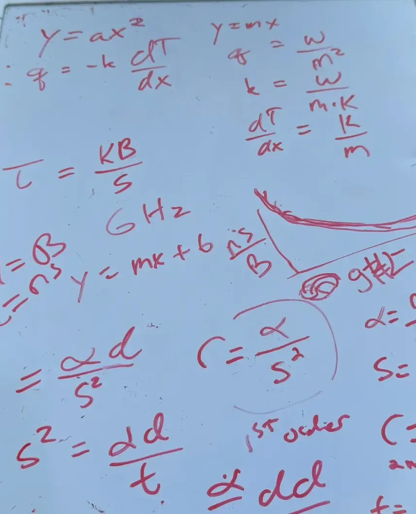 A photo of a whiteboard filled with red handwritten equations, unit analysis, and rough sketches related to engineering and mathematics.